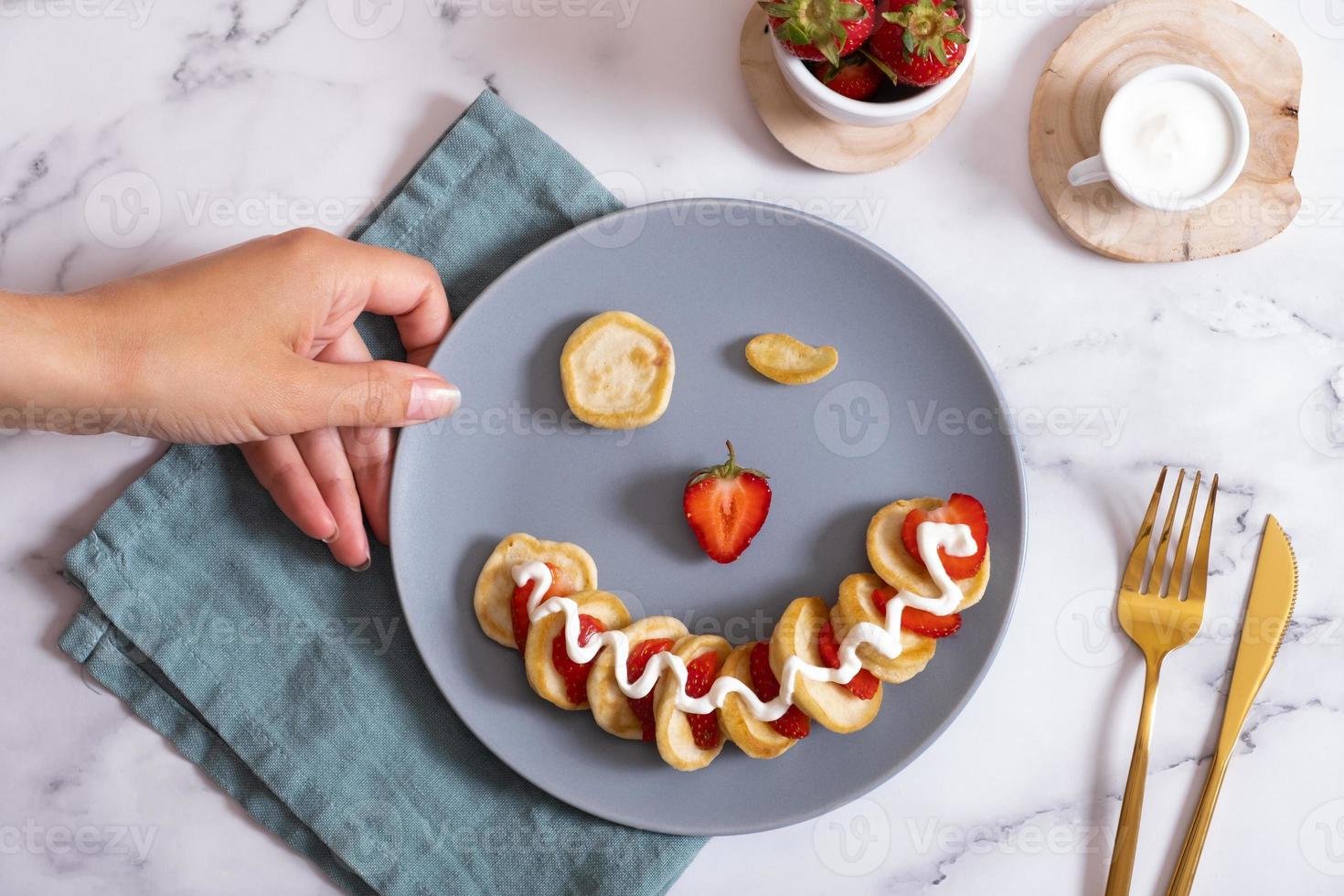 Small pancakes with strawberries in the original serving in the form of a smiley face. Top view. Flat lay photo