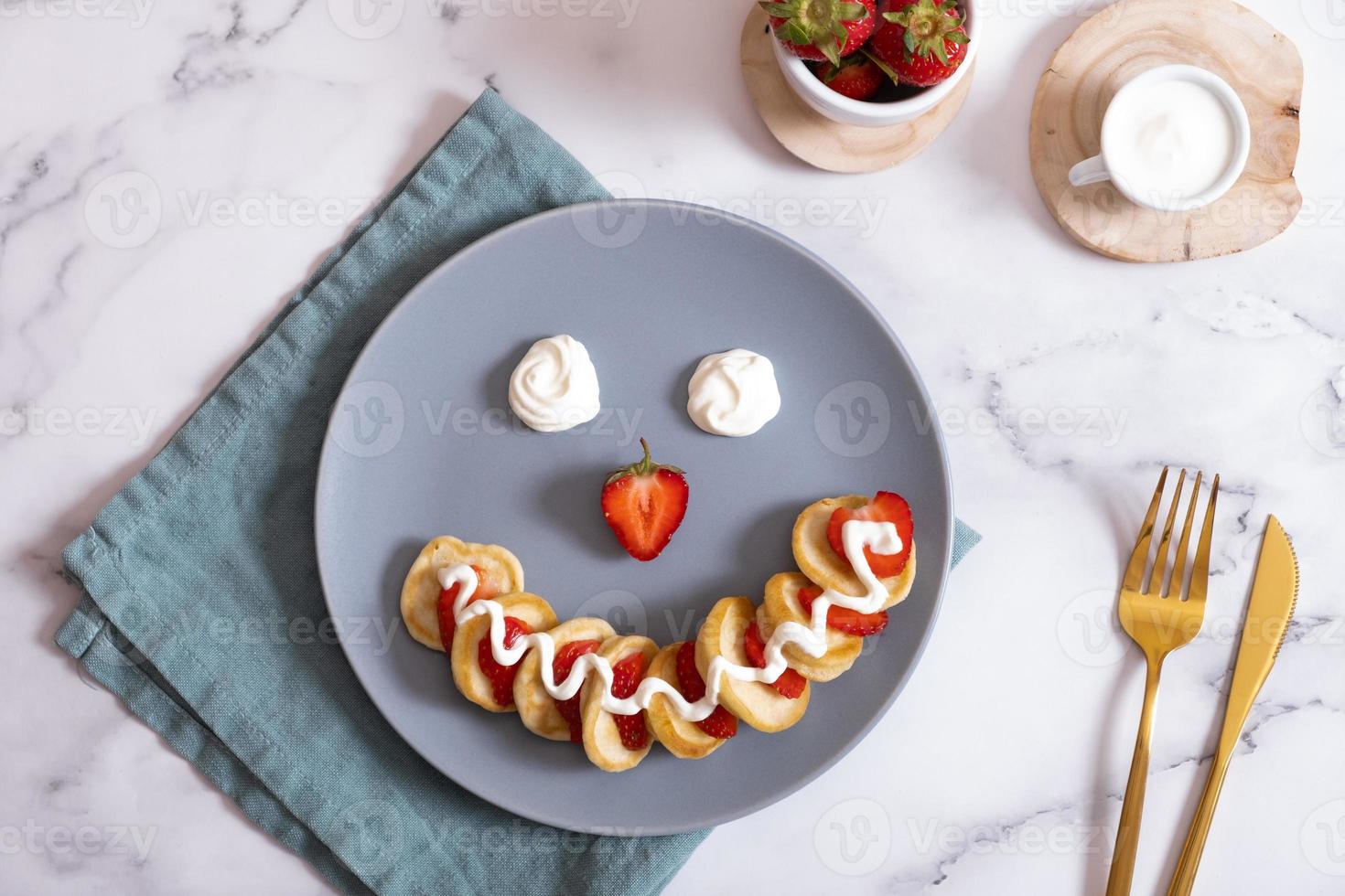 Small pancakes with strawberries in the original serving in the form of a smiley face. Top view. Flat lay photo