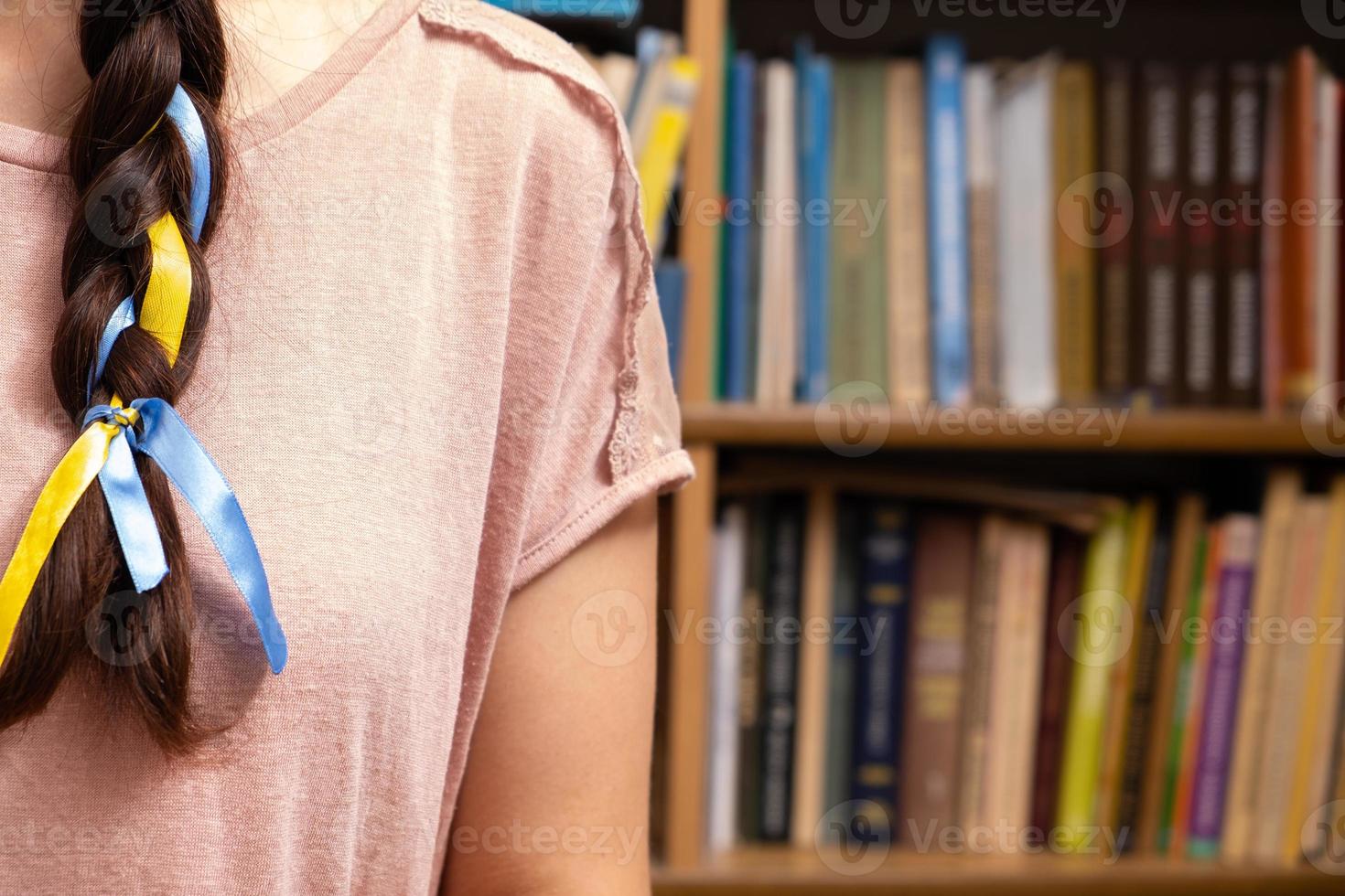 A fragment of a woman's braid with a yellow-blue ribbon on the background of books photo