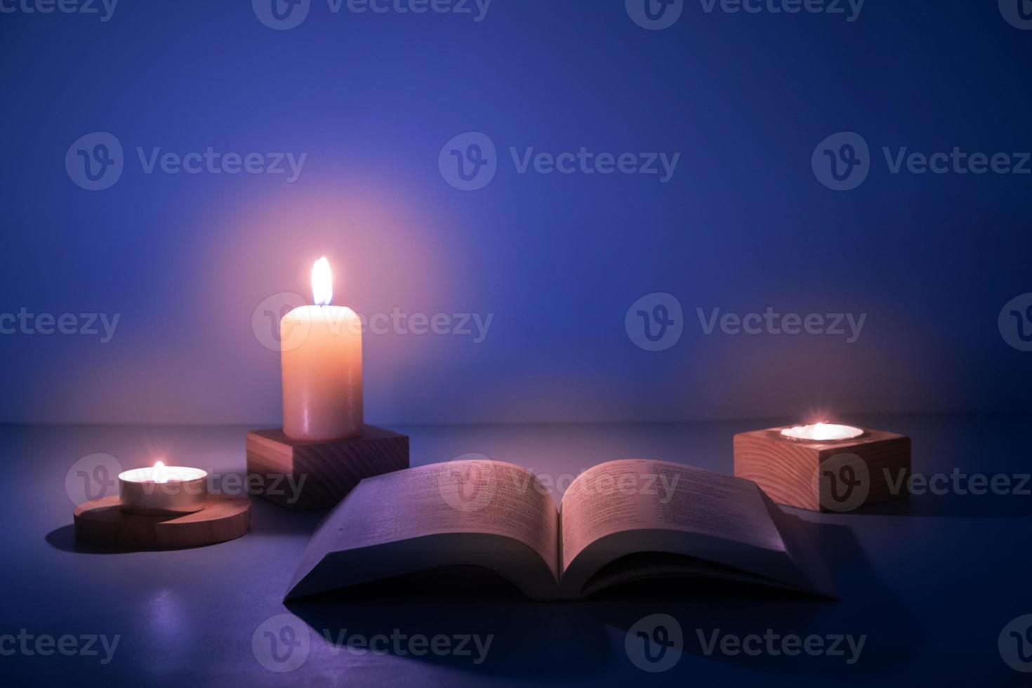 Open Christian Holy Bible with candles lighting on blue background