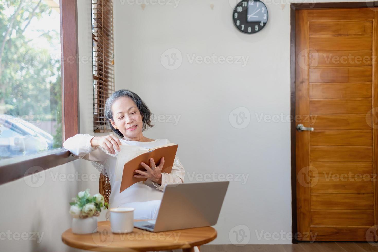 Elderly women sit and relax, stressed, watching series on laptops, reading and taking notes in notebooks and sipping tea happily inside the house with the brightest light and fresh air. photo