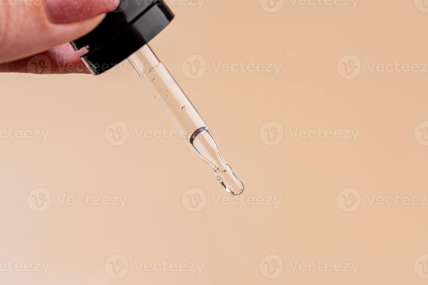 female hand with Dropper of essential oil, aromatherapy essence, beauty serum or medicinal liquid on beige background. Unbranded bottles for your design. photo