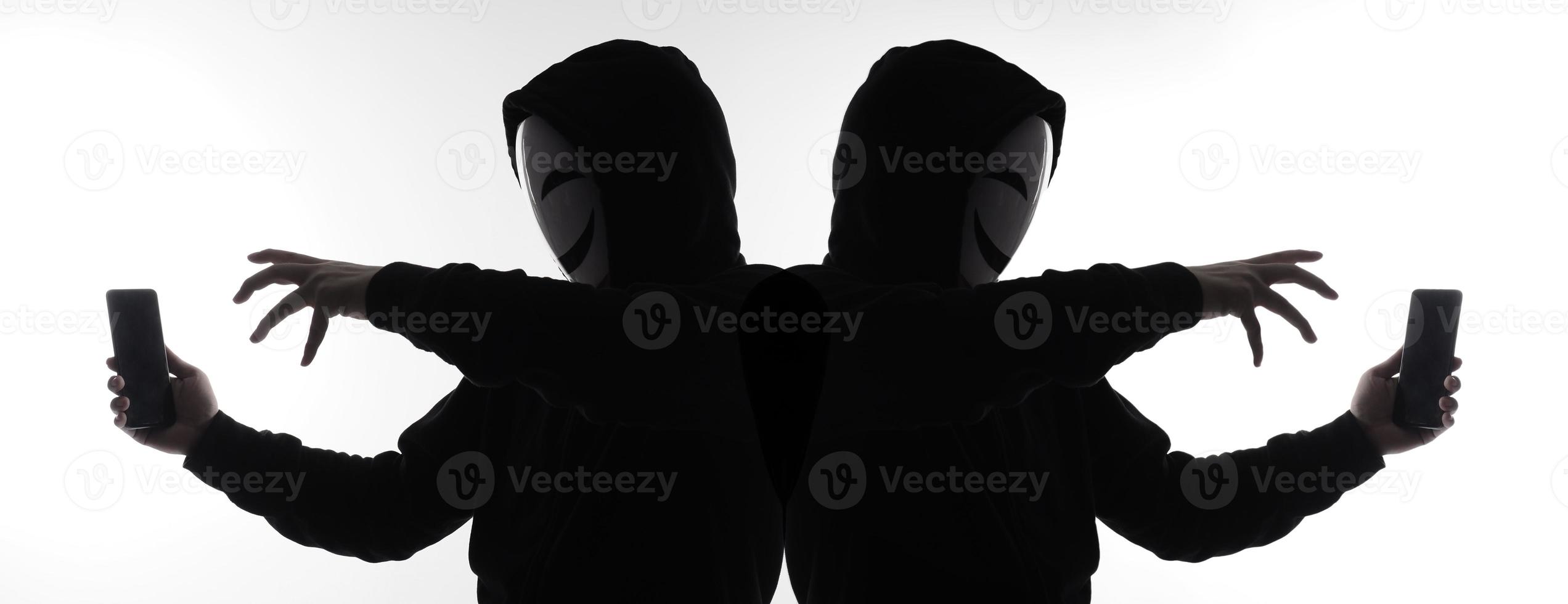 Hacker Anonymous and face mask with smartphone in hand. Man in black hood shirt holding and using mobile phone on white background. Represent cyber crime data hacking or stealing personal data concept photo