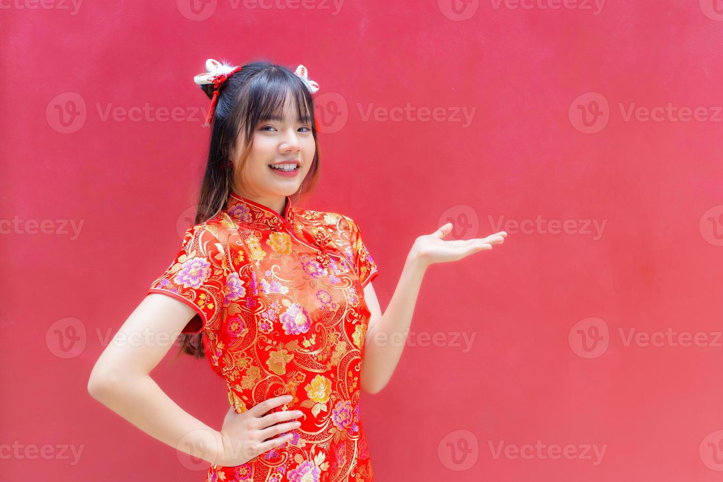 linda chica asiática con pelo largo que usa un rojo cheongsam el del año nuevo chino mientras muestra su mano para presentar algo sobre un fondo rojo. 19578092