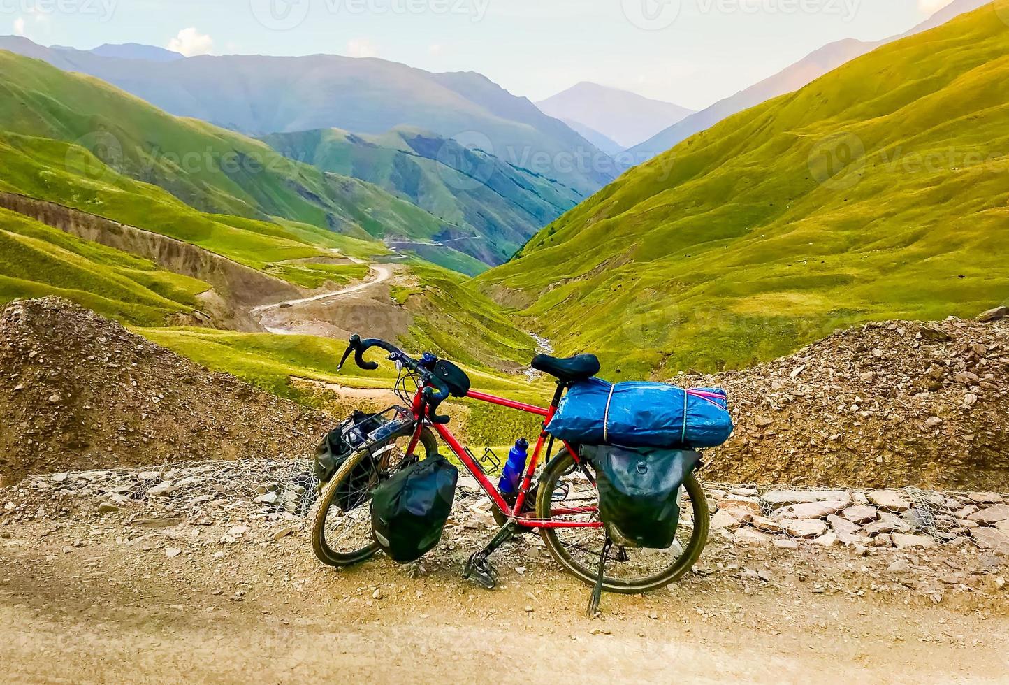 Loaded red touring bicycle with accessories stand in caucasus mountains with beautiful road panorama photo