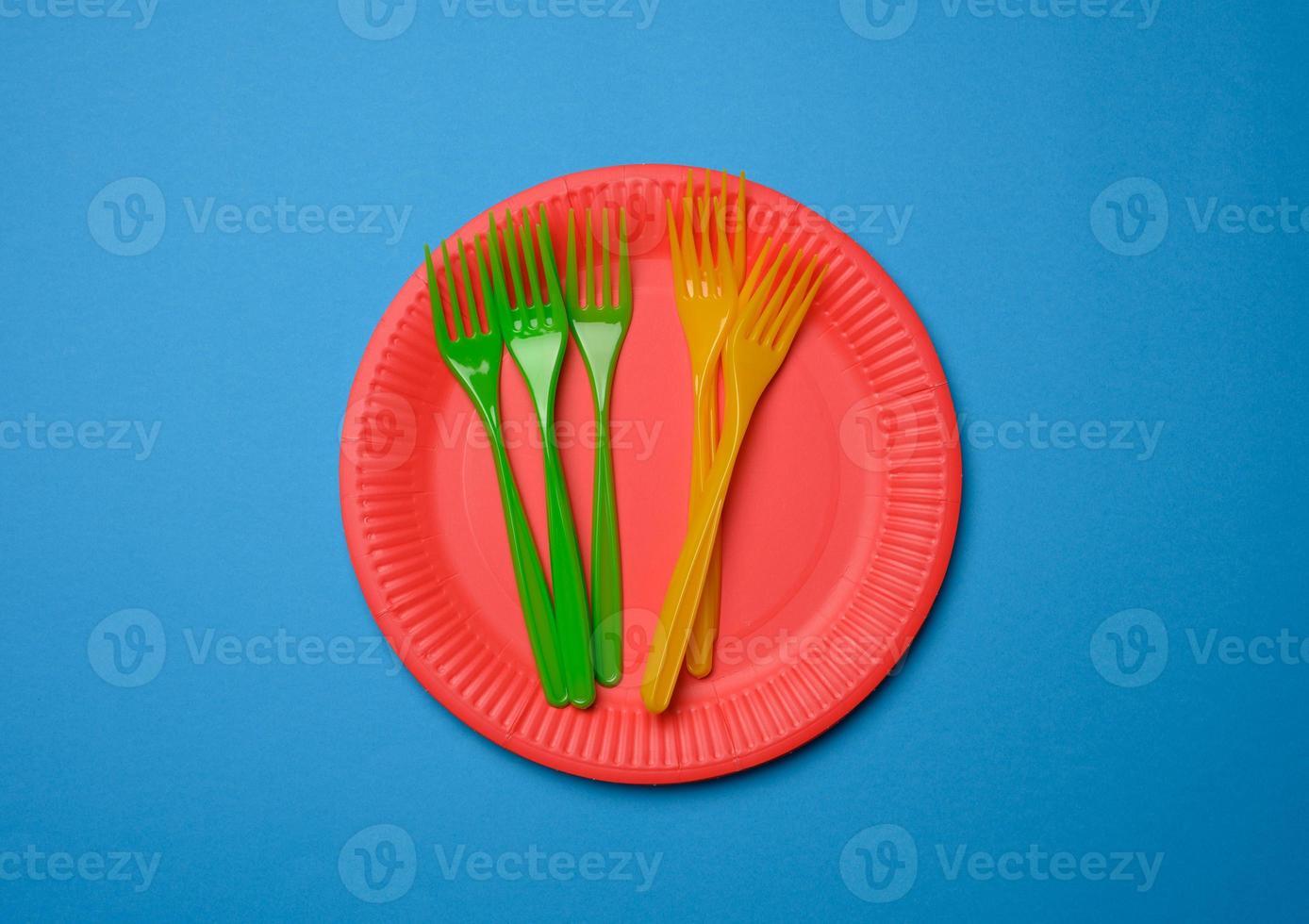 tenedores de plástico verde, naranja y platos desechables de papel rojo vacíos sobre un fondo azul foto
