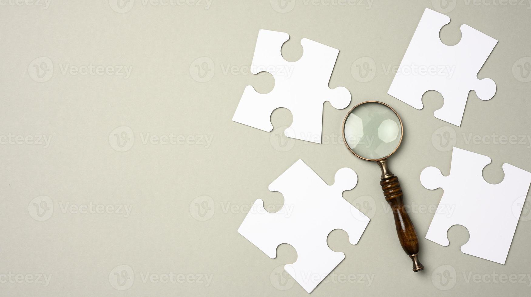 white puzzles around a magnifying glass on a gray background. concept of searching for talented people, recruiting personnel photo