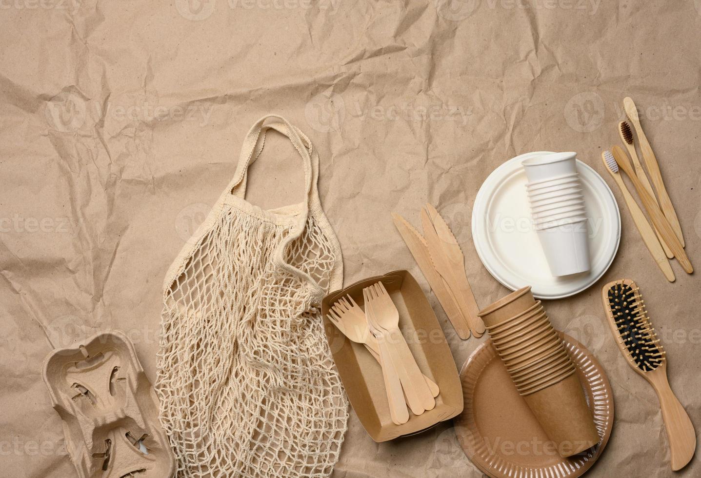 white string bag with disposable paper dishes and wooden forks on brown kraft paper, top view photo