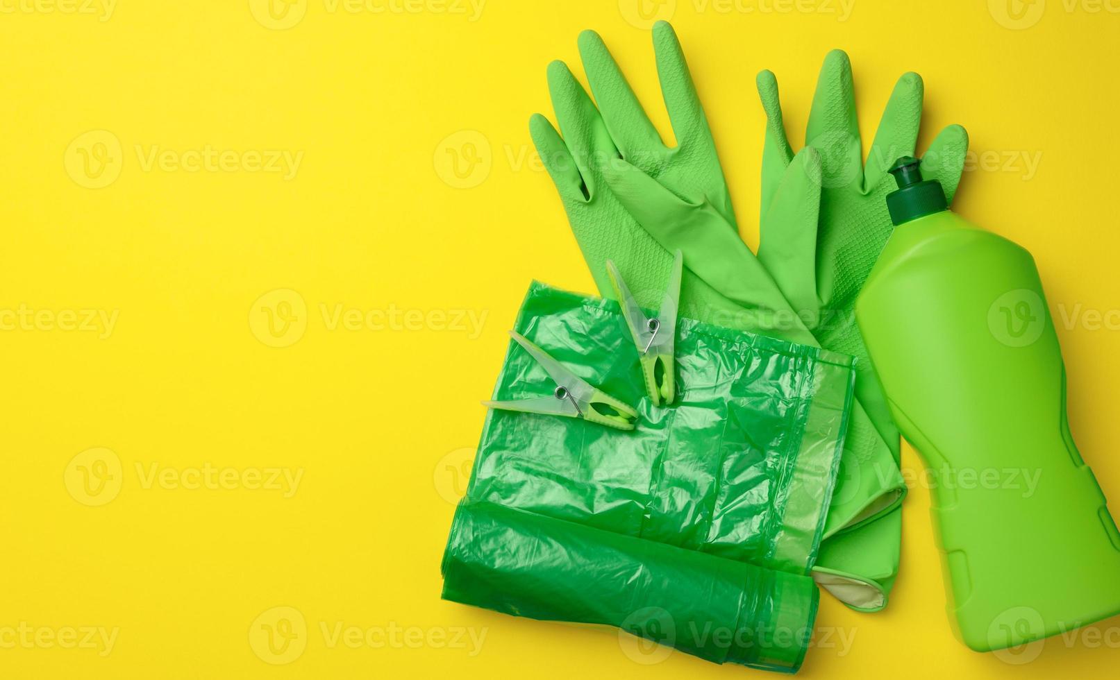 rubber green gloves for cleaning, trash can plastic bag roll and plastic bottle with detergent on yellow background photo