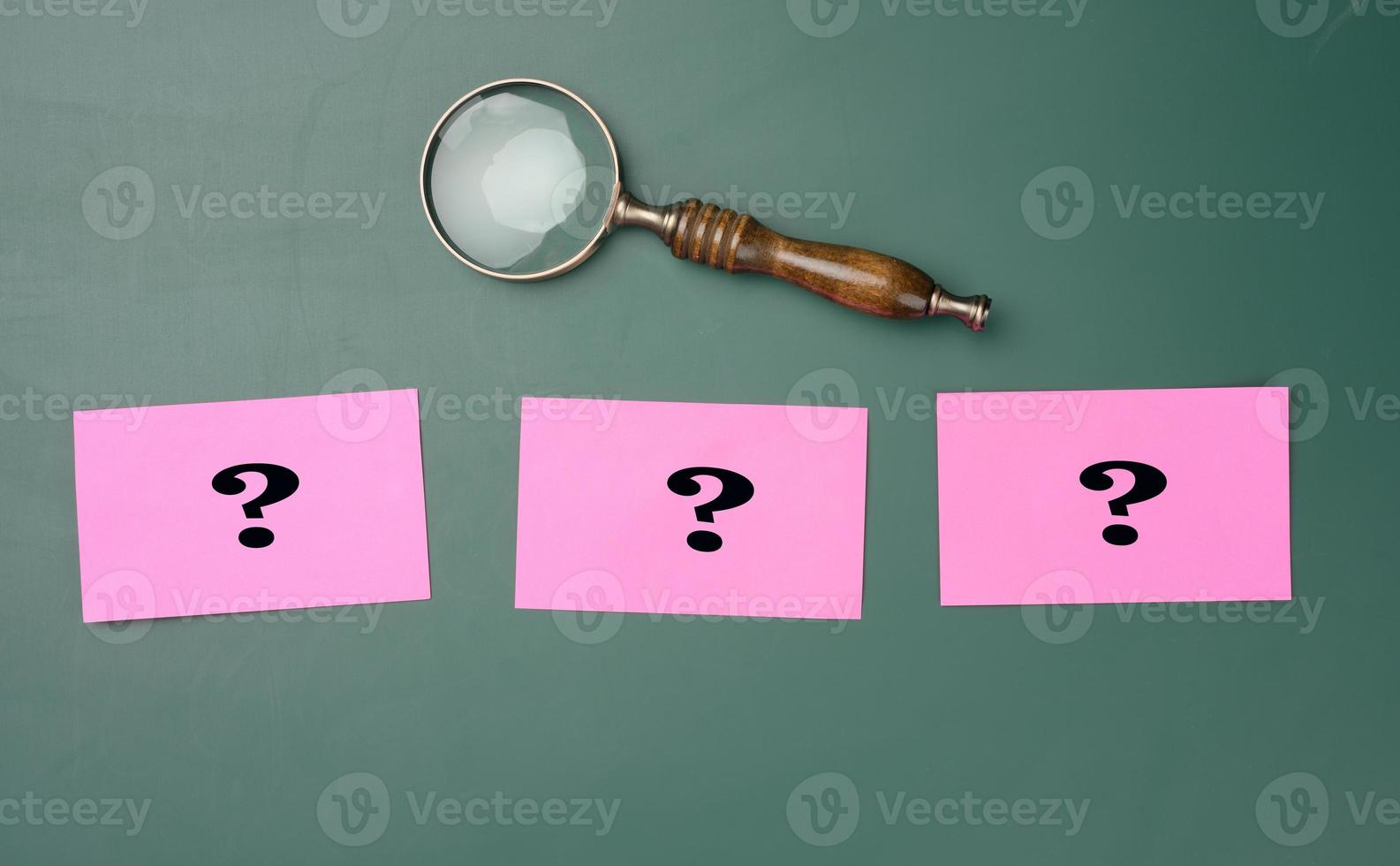 wooden magnifying glass and white chalk drawn question marks on a green chalk board. The concept of finding solutions, true or false. Answers on questions photo