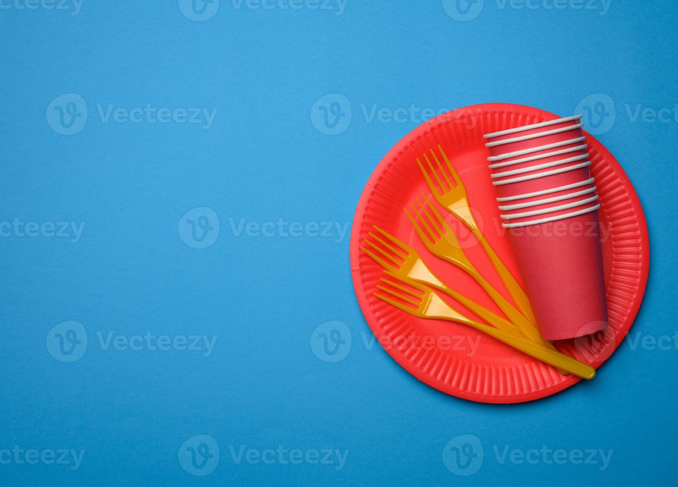 orange plastic forks and empty red paper disposable plates on a blue background photo