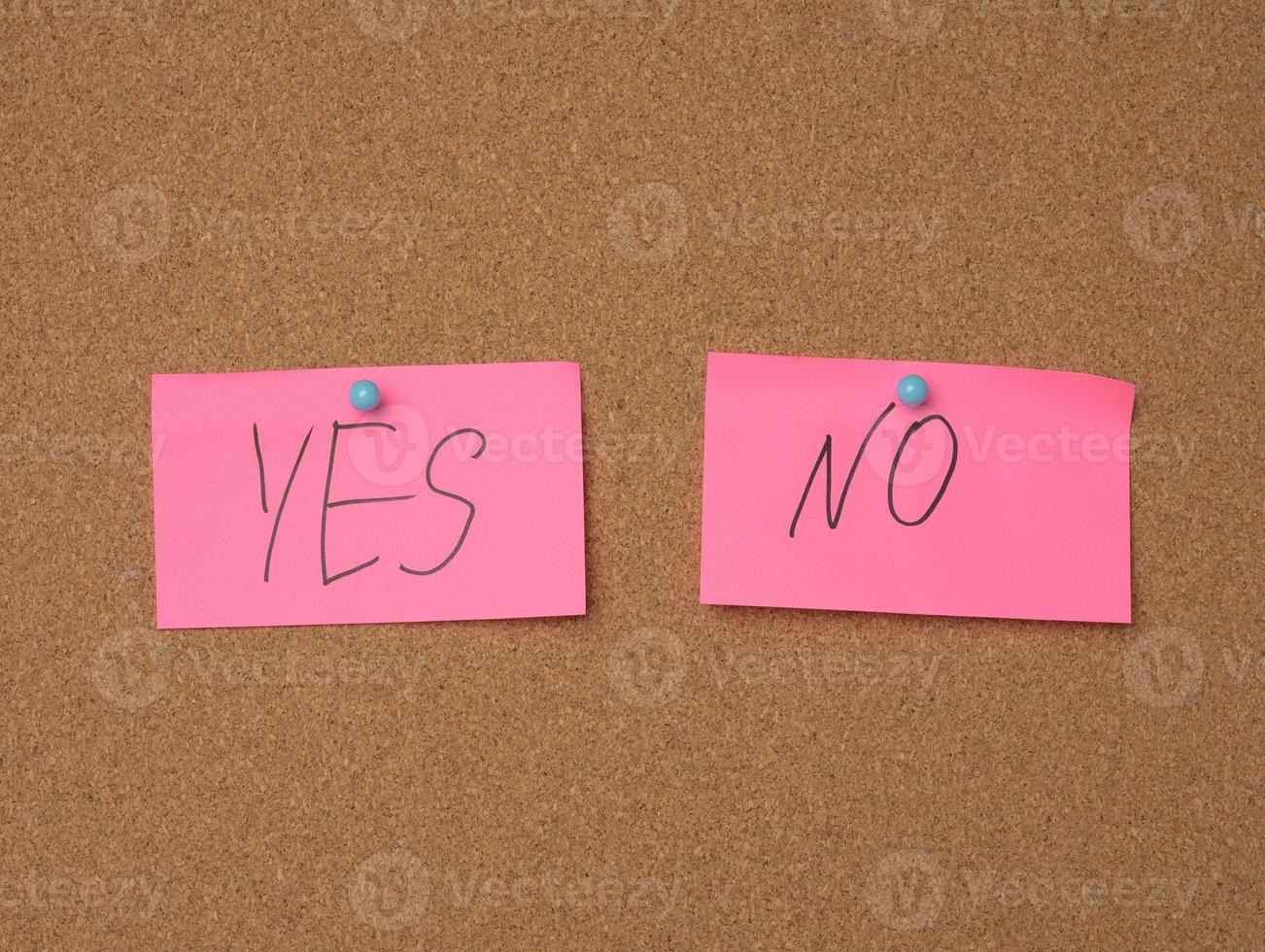 two pink sheets are hanging on a brown cork board, the inscription is yes no photo
