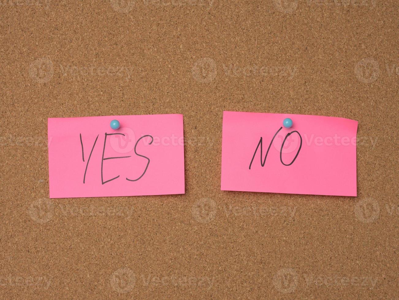 two pink sheets are hanging on a brown cork board, the inscription is yes no photo
