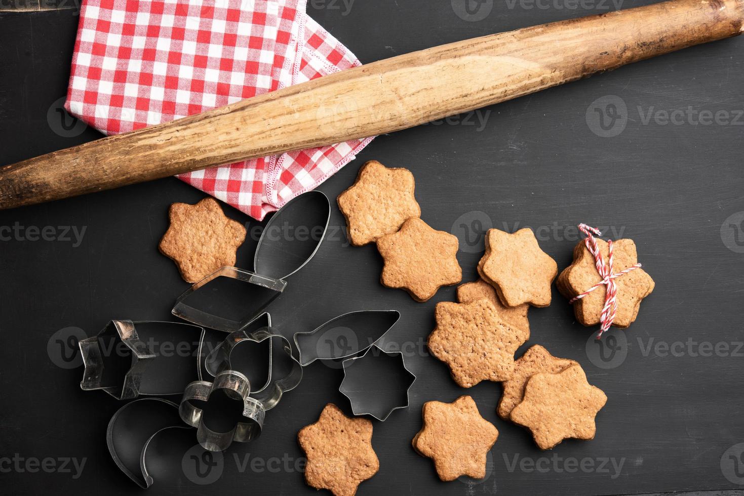 baked star shaped gingerbread cookies, wooden rolling pin and metal cutters on a black table photo