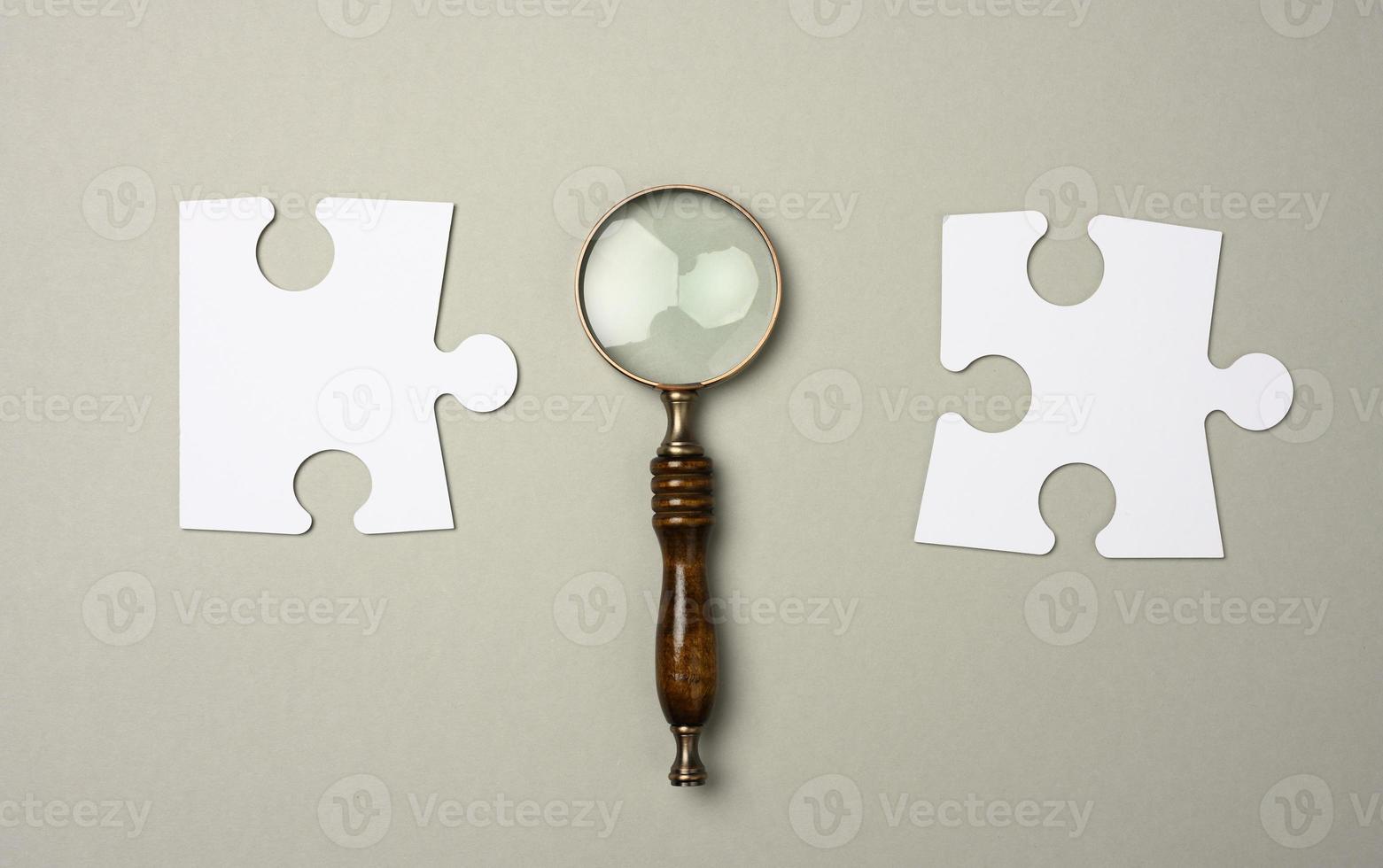 white puzzles around a magnifying glass on a gray background. concept of searching for talented people, recruiting personnel, photo