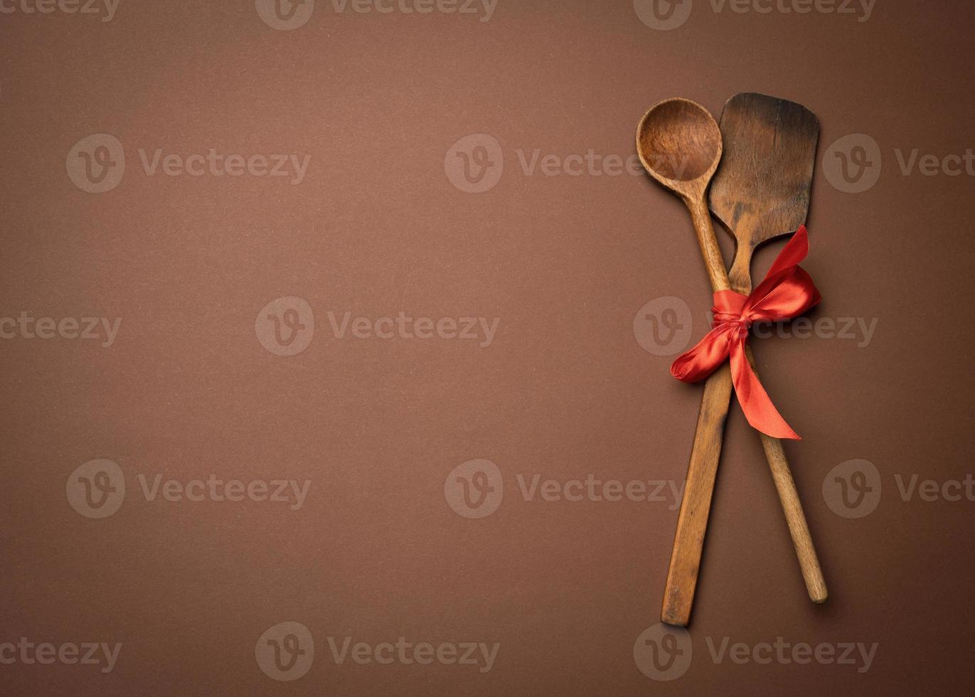 old spoon and spatula tied with red ribbon on a brown background photo