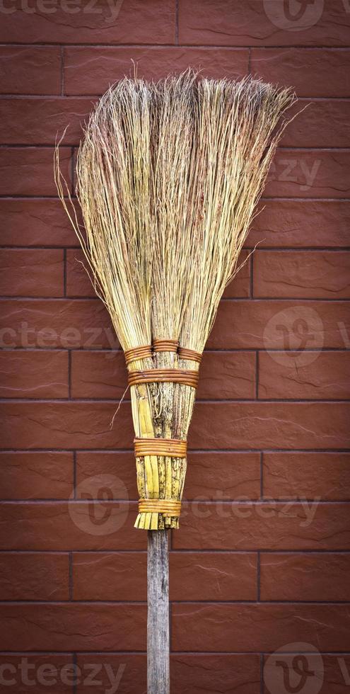 broom on a wooden handle stands near a brick wall photo