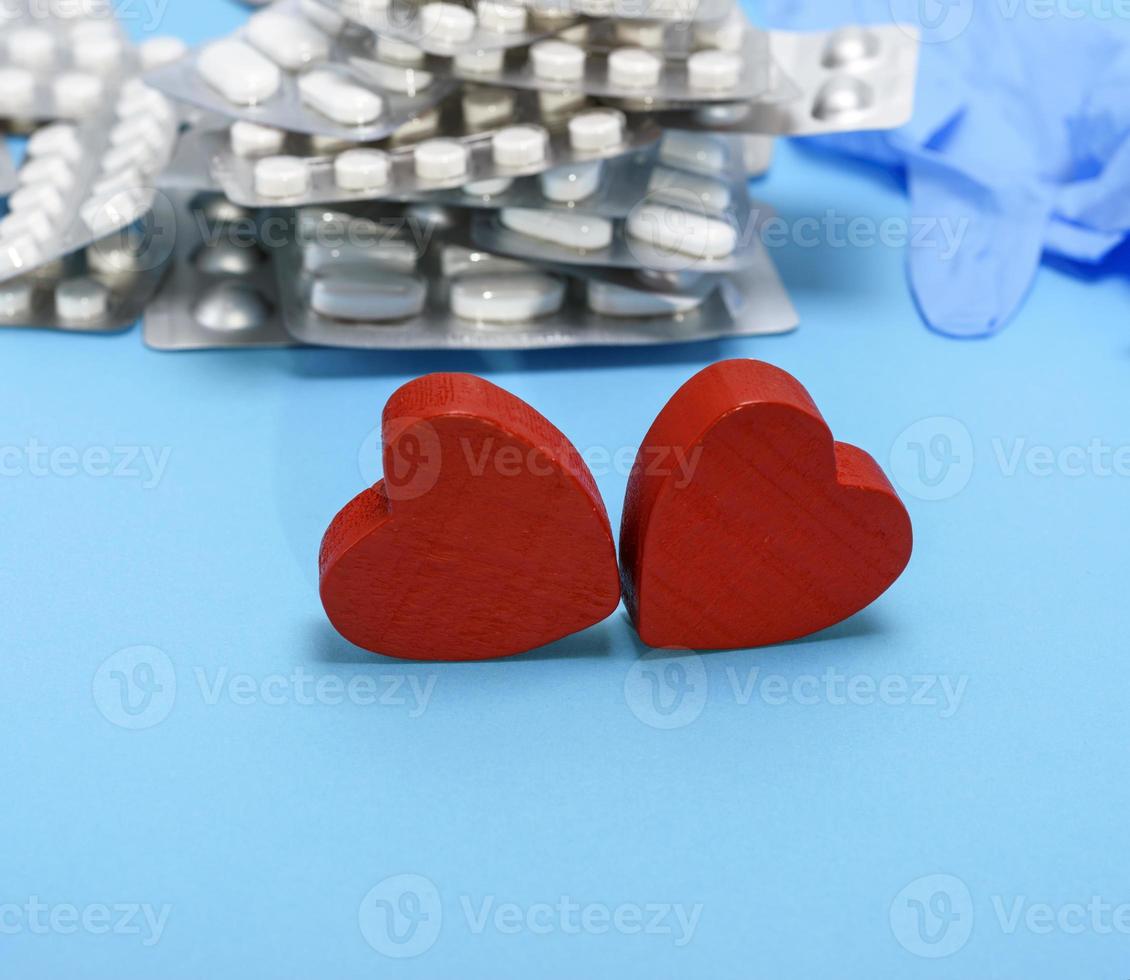 two red wooden hearts on a blue background, behind a stack of pills photo
