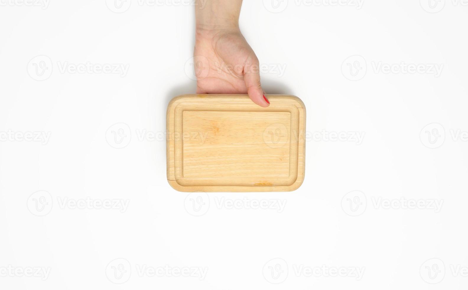 female hand with red manicure holds empty wooden rectangular kitchen chopping board photo