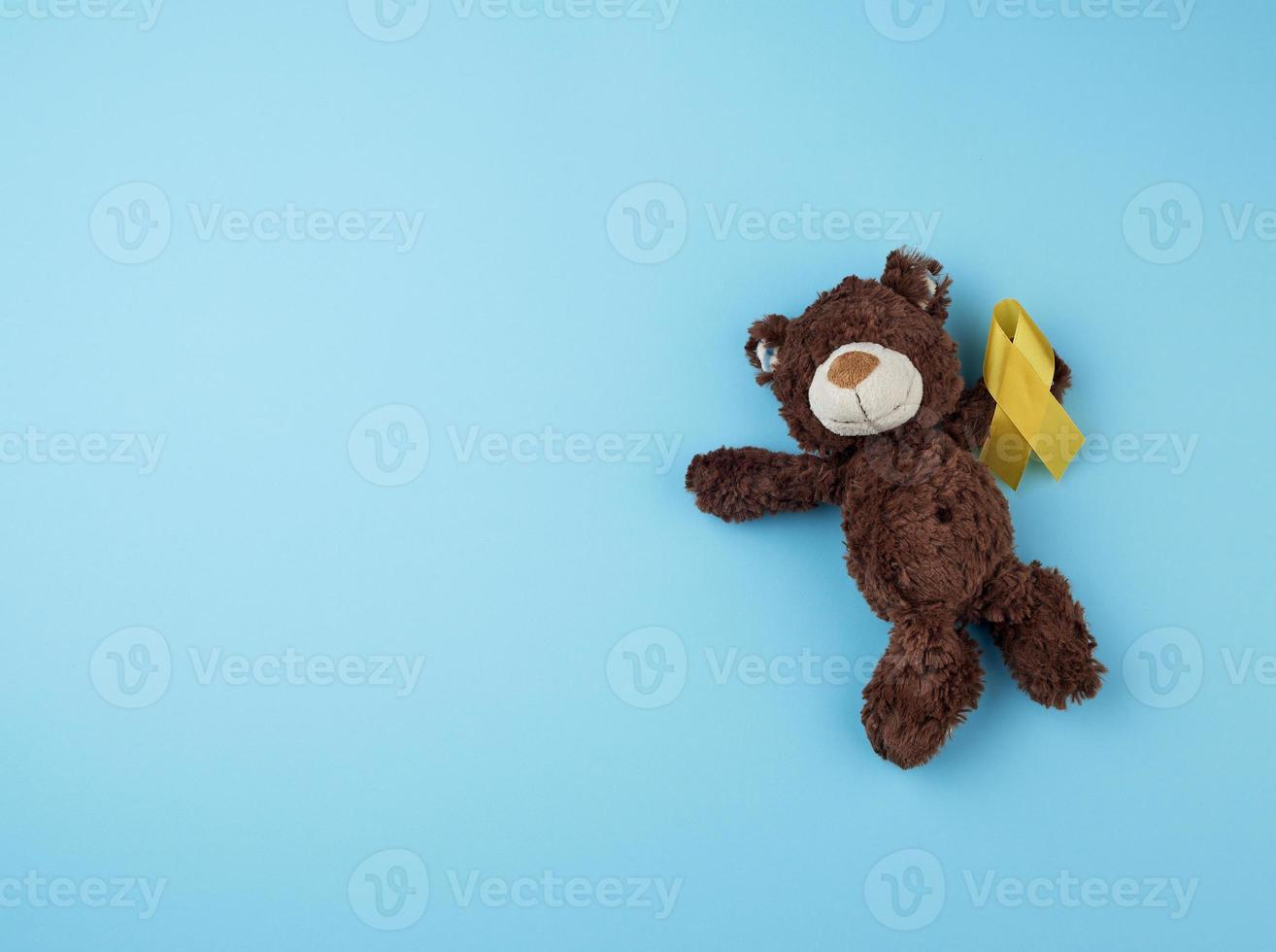 little brown teddy bear holds in his paw a yellow ribbon folded in a loop photo