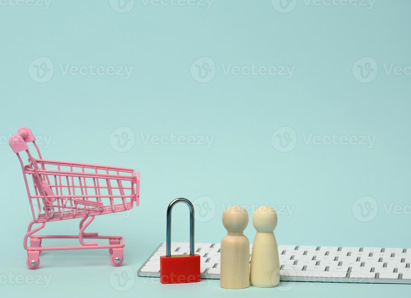 a red metal padlock stands on the keyboard and behind a miniature shopping cart, blue background photo