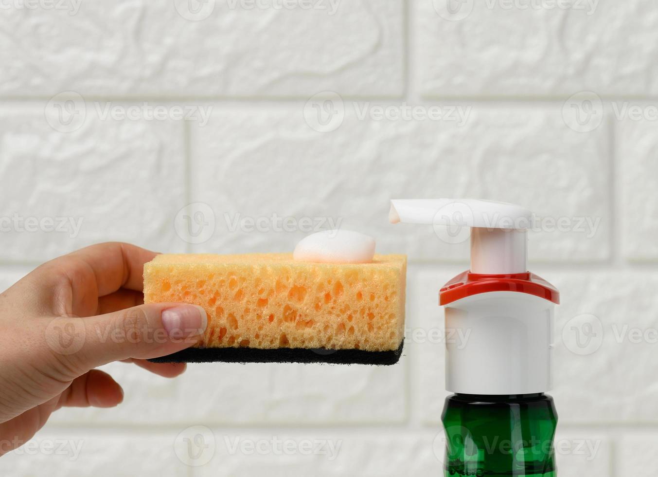 female hand holds kitchen sponge with white foam near plastic dispenser photo