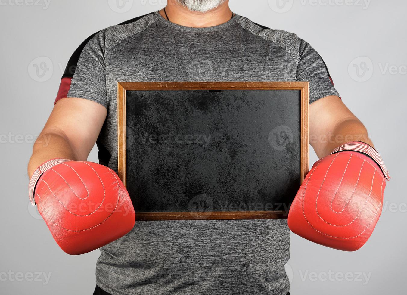 adult athlete in gray uniform and red leather boxing gloves holding a blank black frame photo