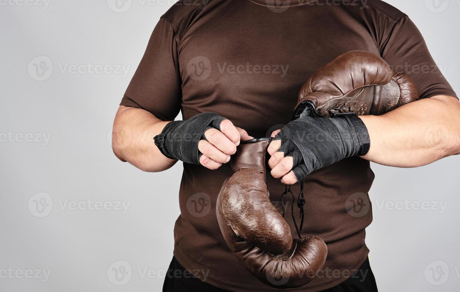 young man stands and puts on his hands very old vintage brown boxing gloves photo