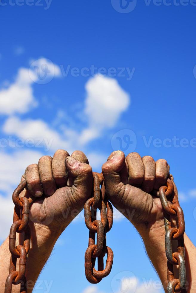 Two men's hands in the mud hold a rusty metal chain photo