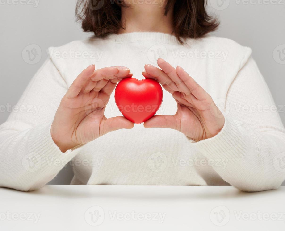 woman in a white sweater holding a red heart, the concept of love and kindness. Donation photo