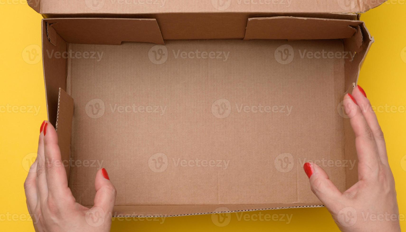two female hands hold open paper box on a yellow background photo