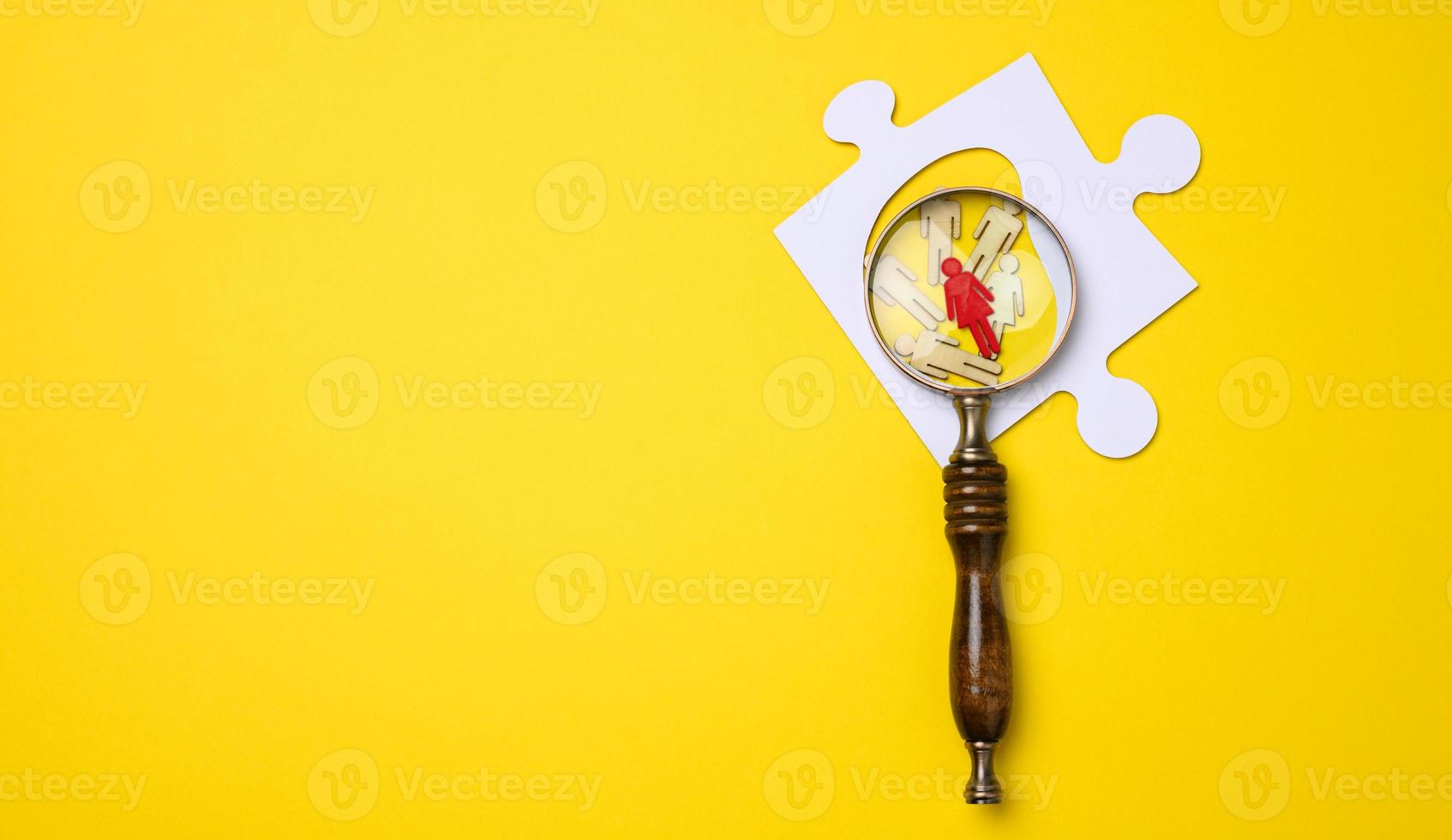 wooden little men lie and a wooden magnifier on a yellow background. concept of searching for talented and unique people photo