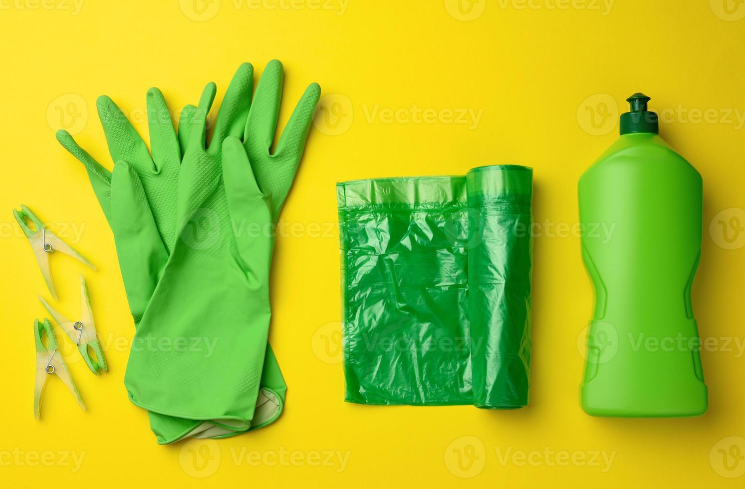 rubber green gloves for cleaning, trash can plastic bag roll and plastic bottle with detergent on yellow background photo