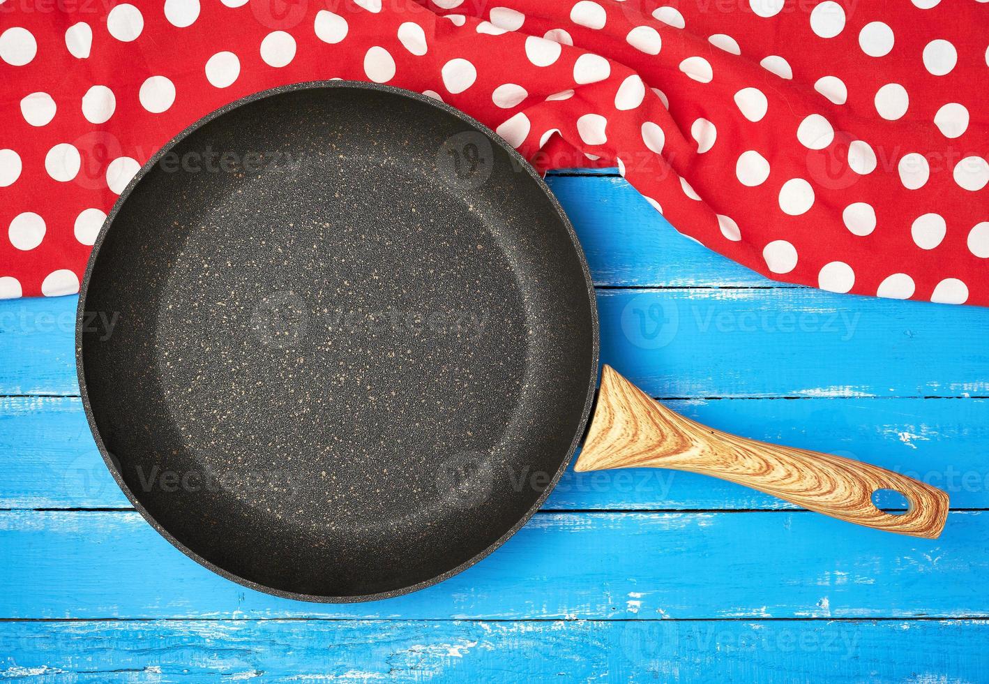 empty black round nonstick frying pan with handle on blue wooden background with red napkin photo