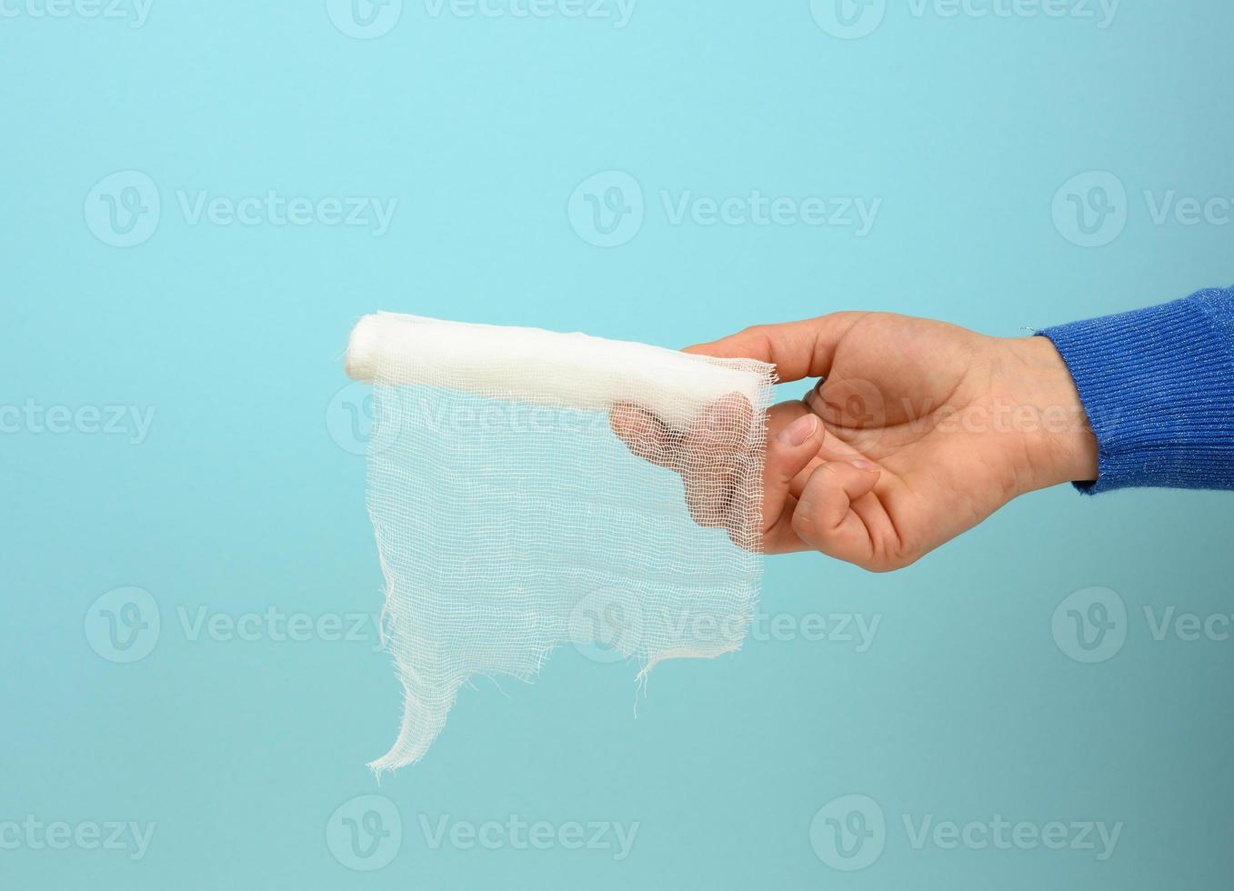 female hand holds white gauze bandage for bandaging limbs, blue background photo