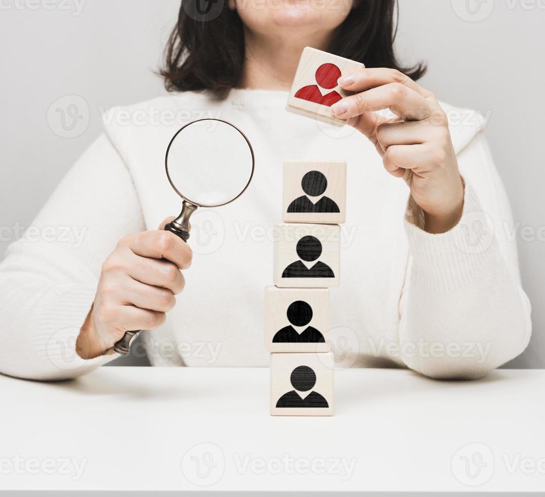 woman holding a magnifying glass and wooden cubes on a white table. Personnel recruitment concept, talented employees. Career advancement photo