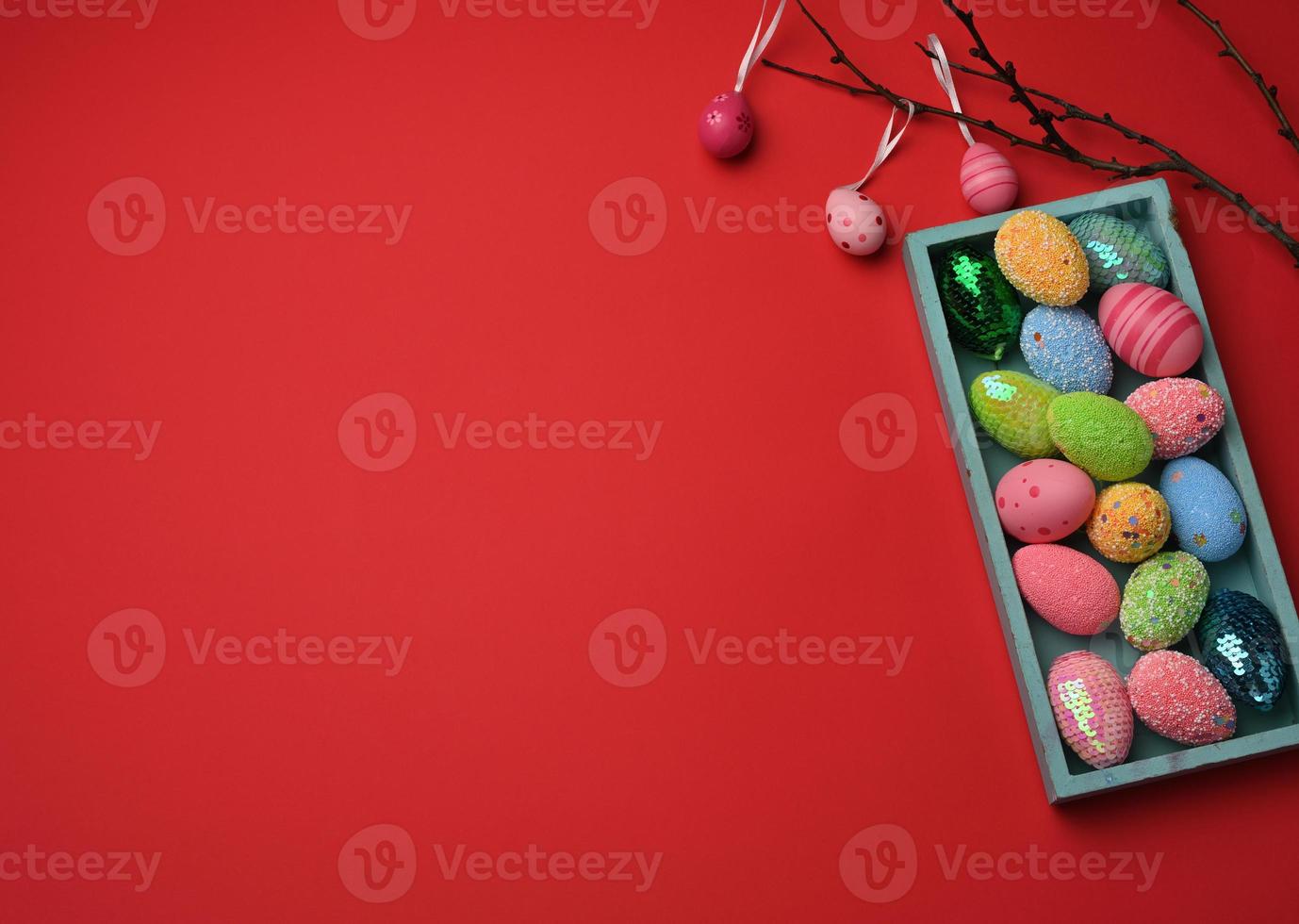 decorative multicolored easter eggs in a wooden box on a red background photo