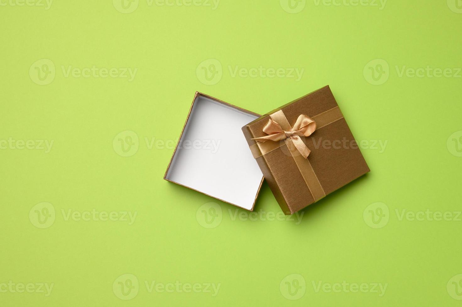 empty square golden box with cardboard bow on green background photo