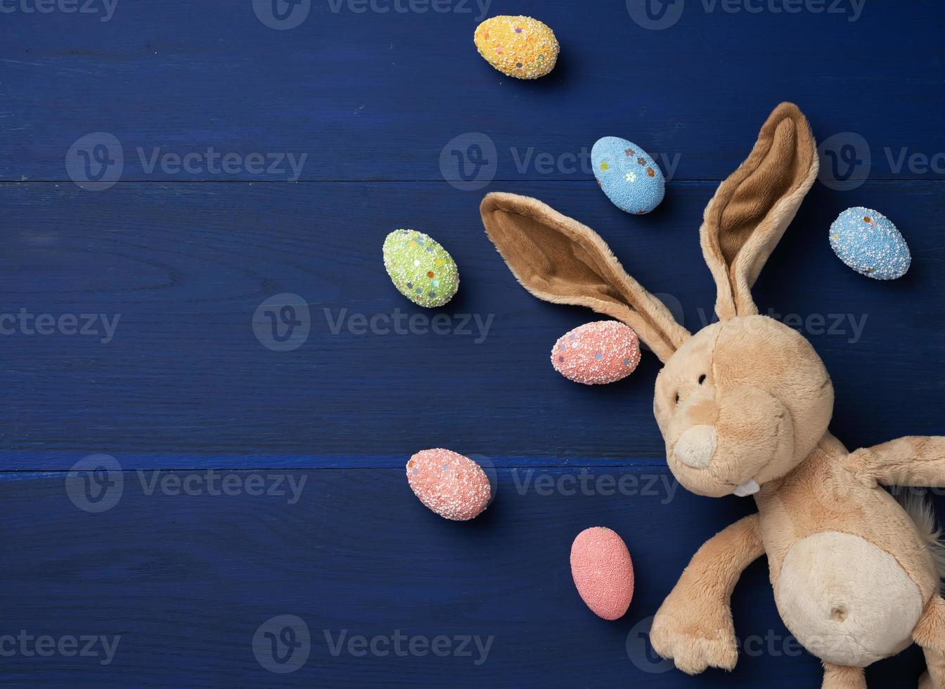 huevos de pascua decorativos y juguete de conejo de peluche suave con orejas largas sobre un fondo azul foto