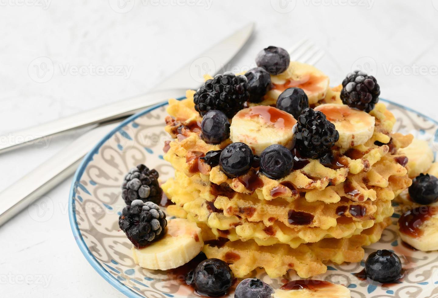 stack of baked Belgian waffles on a round plate with berries on a white table, delicious breakfast photo