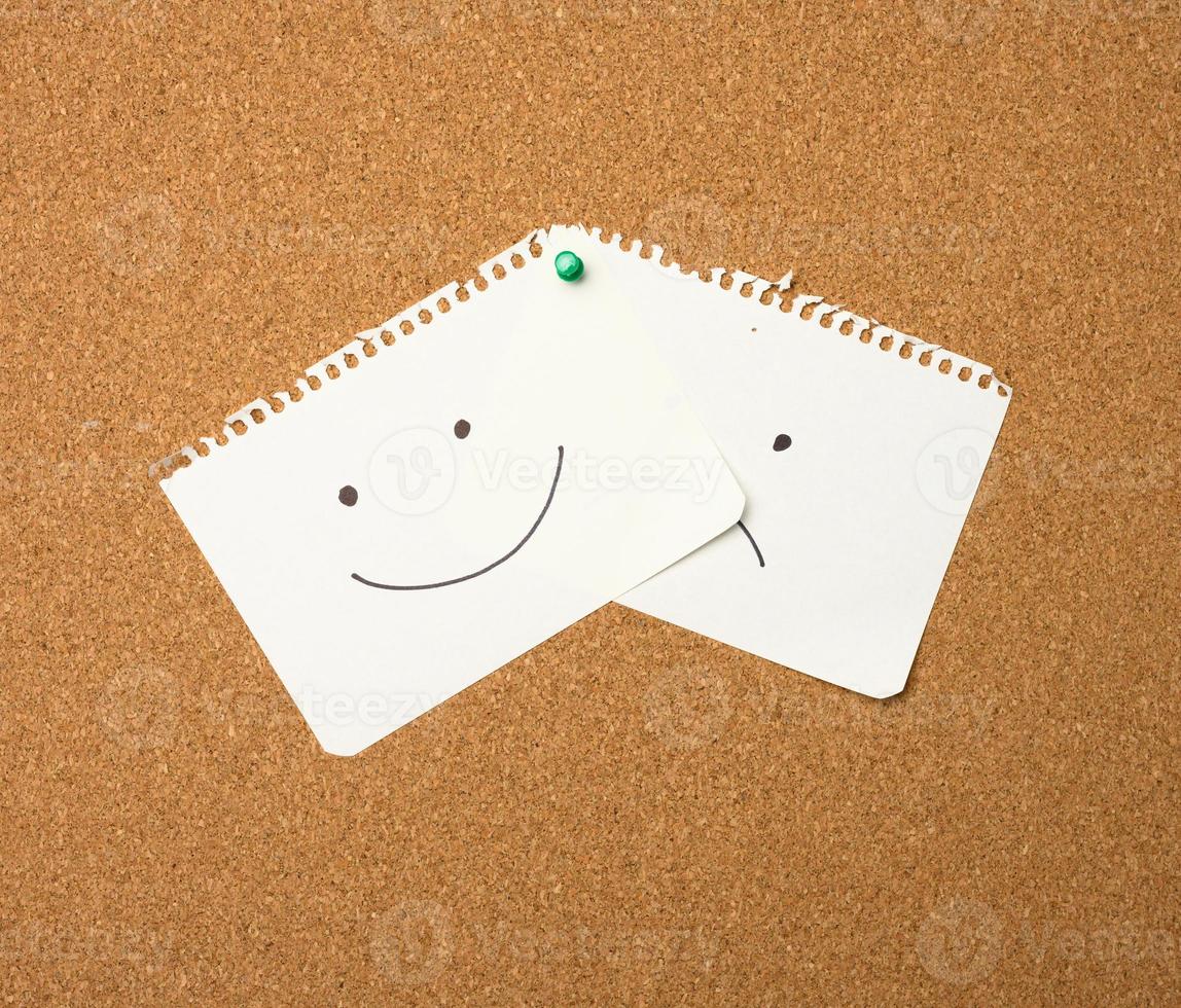 two paper leaves with a smile and a sad emotion attached with a button on a brown board photo