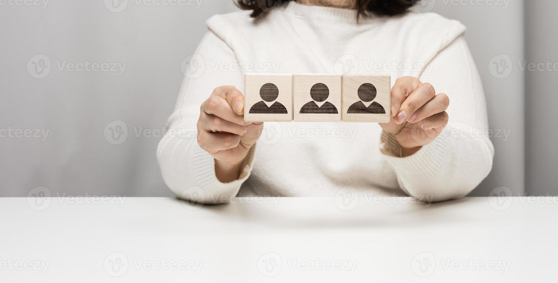 woman sits at a table and holds wooden cubes. The concept of recruiting a team in business, finding talented employees. Leader in a group of people photo