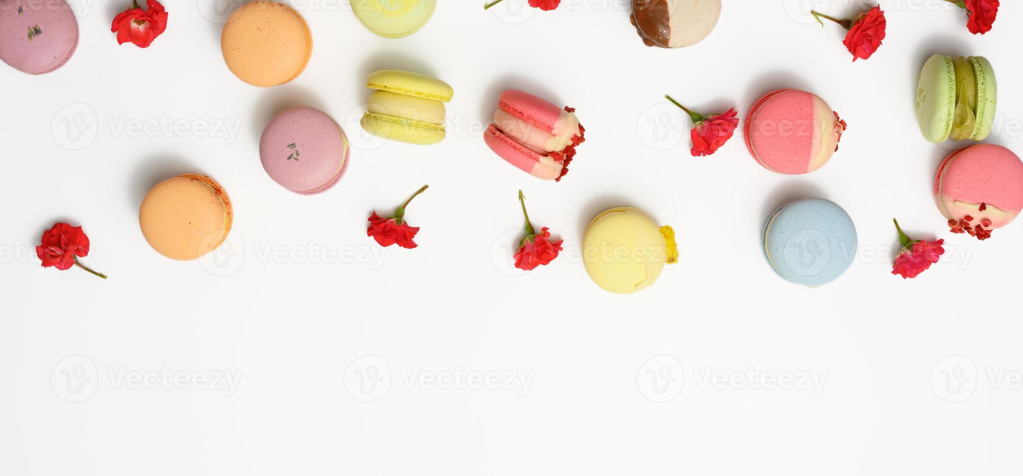 baked macarons with different flavors and rosebuds on a white background photo