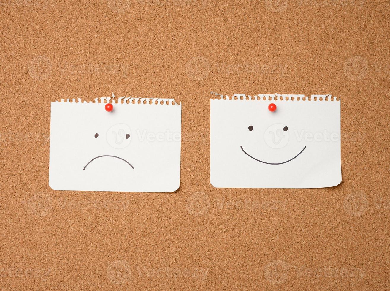 two paper leaves with a smile and a sad emotion attached with a button on a brown board photo