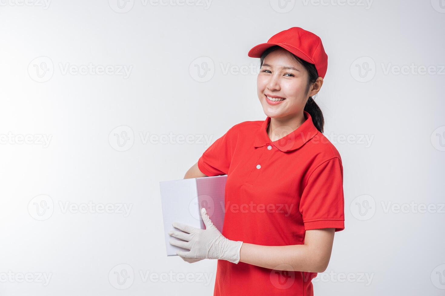 Image of  young delivery man in red cap blank t-shirt uniform standing with empty white cardboard box isolated on light gray background studio photo