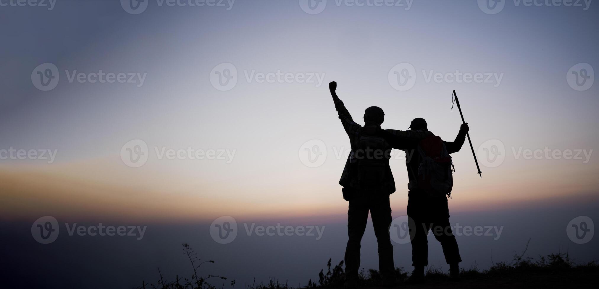 Silhouette of cheering hiking men open arms to the sunrise stand on mountain photo