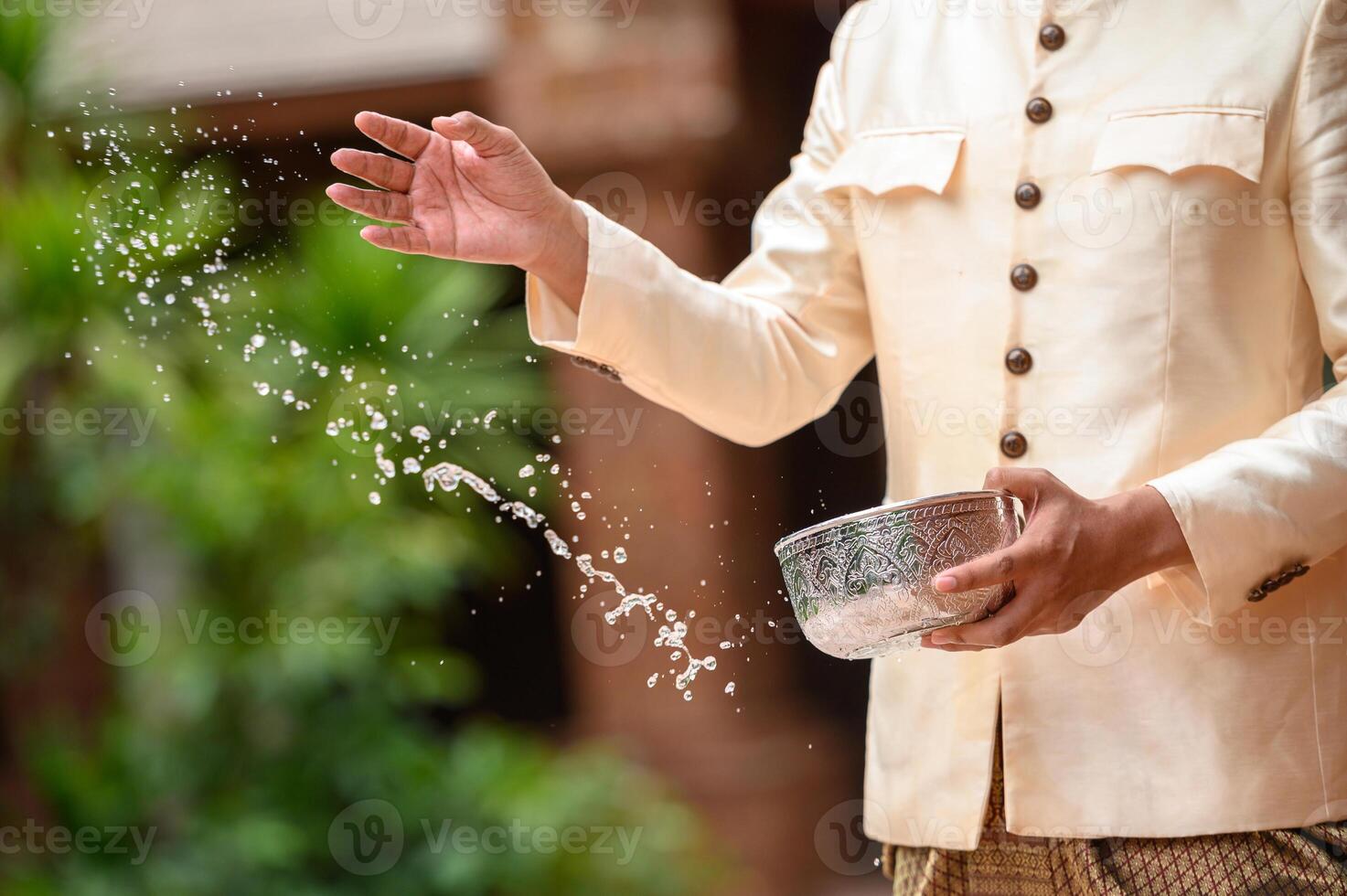 Young man splashing water from bowl on Songkran festival photo