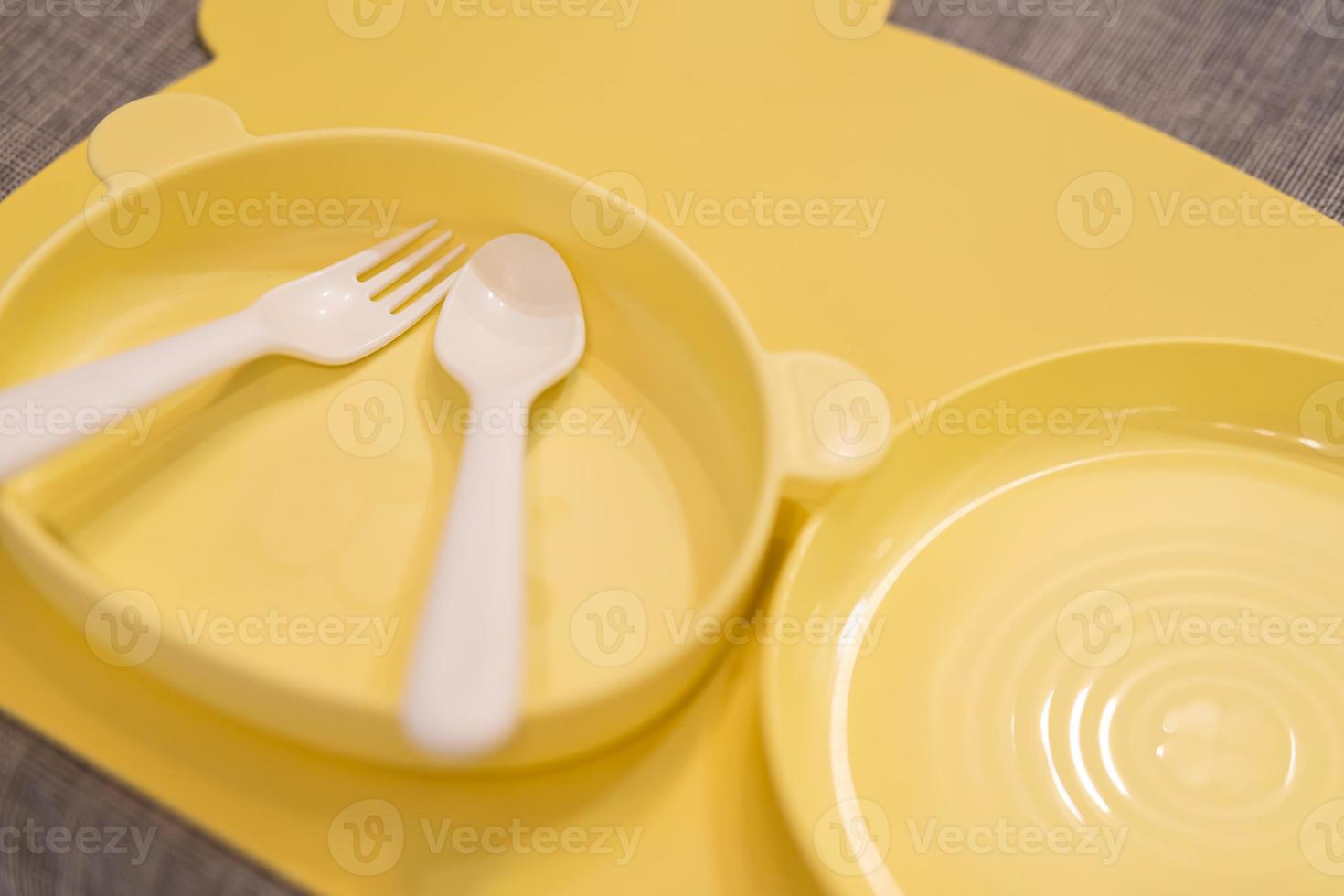 Yellow feeding set. Silicone baby bib, plate, cutlery. Toddler self feeding training, baby weaning concept. Set of plastic dish ware serving baby food. photo