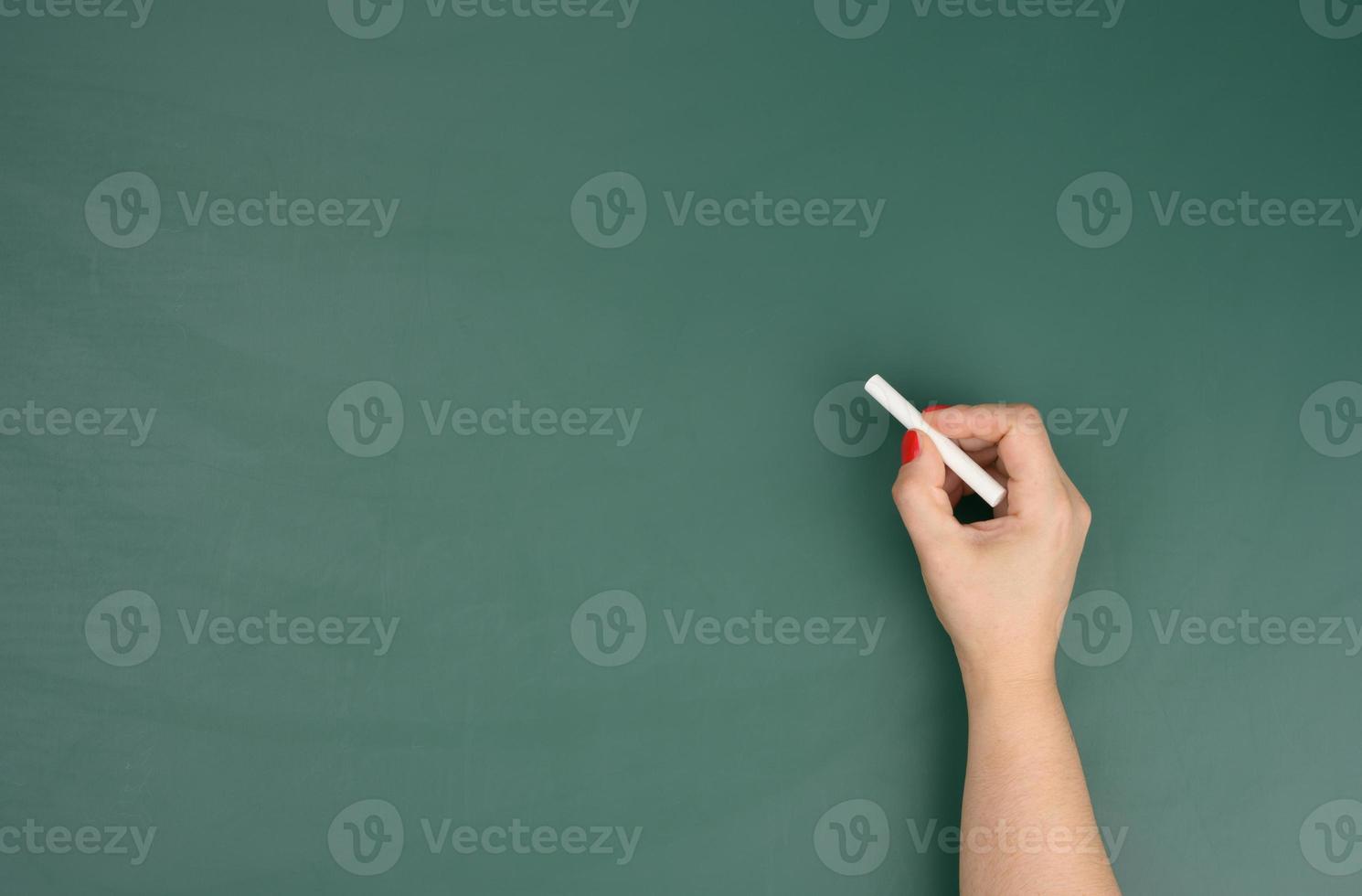 hand holds a piece of white chalk on the background of an empty green chalk board, presentation concept photo