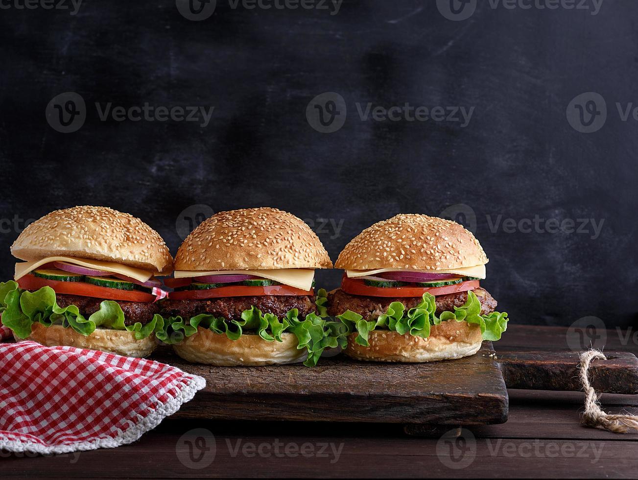tres hamburguesas con verduras en una tabla de madera marrón foto